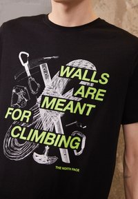 Černé tričko s bílým a neonově zeleným potiskem s nápisem „ZDI JSOU URČENY K LEZENÍ.“ Obsahuje grafiku lezeckého vybavení.