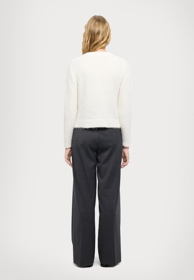 Weißer, flauschiger Pullover mit langen Ärmeln und Rundhalsausschnitt, kombiniert mit dunkelgrauen, weiten Hosen. Einfaches, strukturiertes Design.
