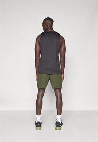 T-shirt sans manches noir avec une coupe décontractée, associé à un short vert olive. L'ensemble est complété par des chaussures de sport noires avec des accents verts.