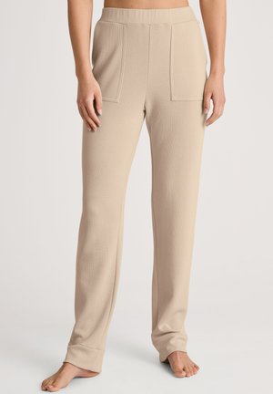 Pantaloni beige a gamba larga realizzati in un tessuto morbido, dotati di due tasche frontali e di una comoda cintura elastica. Leggero texture su tutta la superficie.