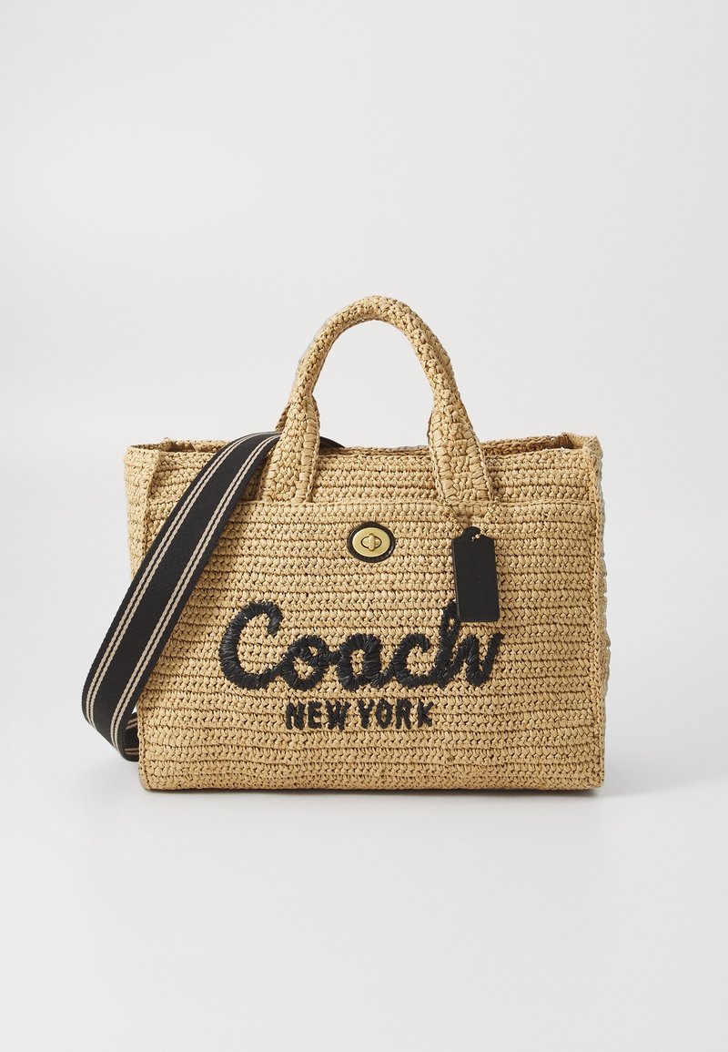 Sac fourre-tout tissé beige Coach New York avec logo noir, doubles poignées, fermoir à tourniquet à l'avant et bandoulière rayée noire.