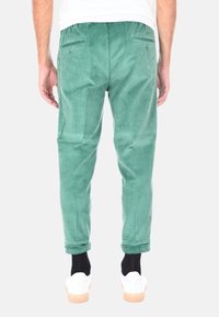 Pantaloni in velluto a coste verde con righe verticali, dotati di due tasche posteriori, vita con coulisse e orli risvoltati.