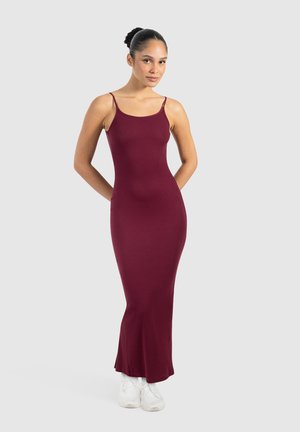 Abito maxi senza maniche color bordeaux con una silhouette aderente. Texture rigata liscia e leggero svaso all'orlo. Abbinato a sneakers bianche.