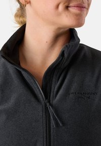 Giacca in pile grigio scuro con zip e colletto alto, caratterizzata da una texture liscia e un logo discreto sul petto. Zip con linguetta in tessuto.