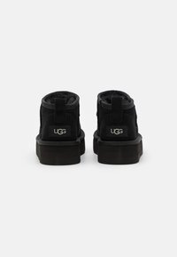 Botas de tobillo UGG negras con un suave forro de lana, material exterior duradero, suela de goma plana y logotipo de UGG en el talón.