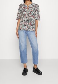 Blusa con motivo floreale e scollatura a chiave, maniche corte a sbuffo, abbinata a jeans azzurri e mocassini neri con plateau.