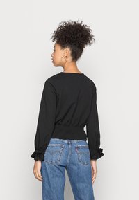 Black long-sleeve top with gathered waist and ruffled sleeve hems, paired with blue high-waisted jeans featuring back pockets and stitching details.