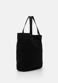 Black canvas tote bag with two shoulder straps, rectangular shape, and a minimalistic design. Features a side label detail.