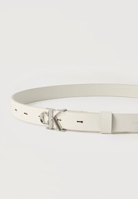 Λευκή δερμάτινη ζώνη με ασημένια αγκράφα "cK" και αρκετές τρύπες για ρύθμιση σε απλό λευκό φόντο.