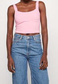 Top corto rosa con escote cuadrado y tirantes anchos, combinado con unos vaqueros de mezclilla azules de cintura alta con un acabado desgastado.