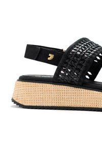 Sandalias de plataforma negras con parte superior de textil trenzado, plantilla intermedia de fibra natural texturizada y herrajes en color dorado. Correa ajustable en el talón.