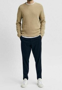 Pullover beige lavorato a maglia con scollo rotondo, abbinato a pantaloni blu navy e sneakers bianche, creando un look casual e coordinato.