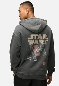 Grå hoodie med dragsko i huvan, med en Star Wars-grafik på baksidan som avbildar rymdskepp och stänk detaljer. Ribbad muddar och nederkant.