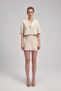 Beige lyhythihainen cropped-paita etutaskuilla, yhdistettynä sopivan korkeavyötäröiseen hameeseen, jota täydentävät beige nauhakenkiä.