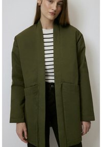 Palton verde măsliniu cu un design lung și drept. Are două buzunare frontale, un guler larg și este asortat cu un top cu dungi alb-negru.