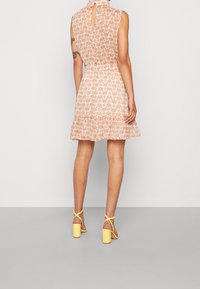 Robe sans manches à motifs floraux avec un dos en trou de serrure, taille froncée et ourlet volanté dans des teintes de rose doux. Associée à des sandales à talons blocs jaunes.