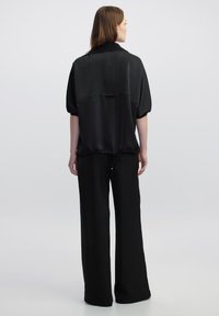 Top nero a maniche corte con una vestibilità ampia, caratterizzato da un orlo con lacci e un colletto. Indossato con pantaloni neri a gamba larga coordinati. Texture morbida.