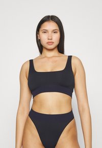 Svart crop-top og høyt liv bukser laget av glatt stoff; har en firkantet utringning og elastisk midje i en kontrasterende mørk nyanse.