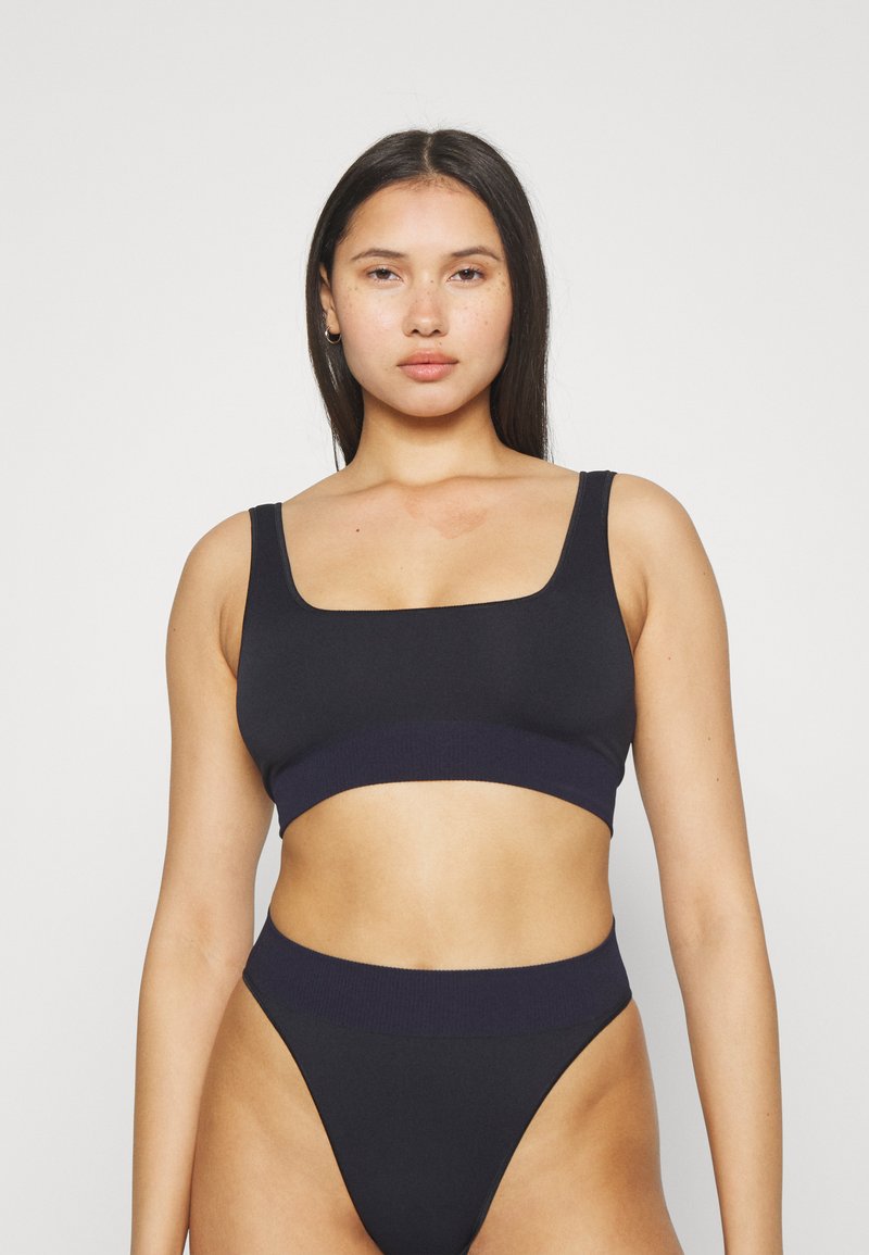 Svart crop-top og høyt liv bukser laget av glatt stoff; har en firkantet utringning og elastisk midje i en kontrasterende mørk nyanse.