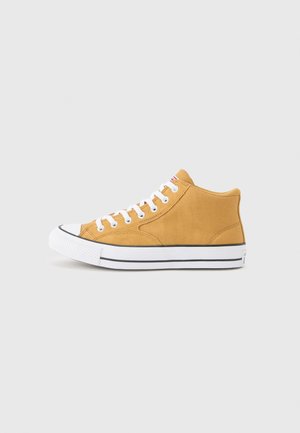 Žltá vysoko členková plátená teniska s bielymi šnúrkami a gumovou podrážkou, s čiernym pruhom okolo podrážky a bielou špičkou.