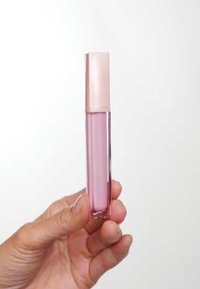 Transluzentes, rosafarbenes Lipgloss in einer hohen, rechteckigen Tube mit einem hellrosafarbenen Deckel. Glatte Textur, gehalten in einer Hand vor einem schlichten Hintergrund.
