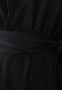 Black fabric dress with a wide belt tied in a knot at the waist, showing gathered material above and smooth fabric below the belt.