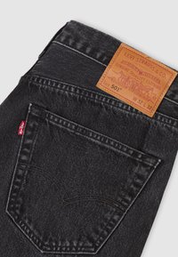 Μαύρα τζιν από denim με δερμάτινο ταμπελάκι που αναγράφει "Levi Strauss & Co." στη μέση, με κλασικό σχεδιασμό πέντε τσεπών και διακριτικές ραφές.