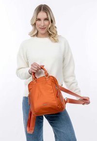 Orange nylon backpack with dual top handles and a detachable strap. Features sleek design, zippered pockets, and a smooth texture.