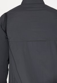 Svart, lätt jacka med texturerad tyg. Har en ståkrage, långa ärmar och en horisontell söm på baksidan.