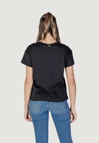 T-shirt nera a maniche corte con scollatura tonda. Realizzata in tessuto morbido, presenta un piccolo logo nella parte posteriore. Design pulito e semplice.