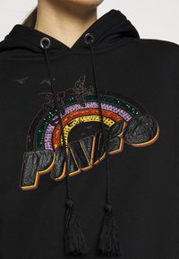 Hoodie noir avec un design arc-en-ciel texturé multicolore orné de strass et d'accents brodés, complété par des cordons de serrage et des glands.