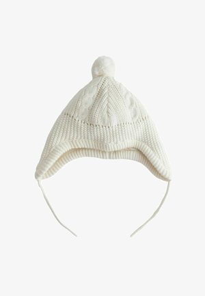 Hvid strikket vinterhat med øreklapper, flettet mønster, kvast på toppen og to snore, der hænger ned.