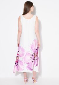 Weißes ärmelloses Kleid mit großen rosa Blumenmotiven am Saum. Glatter Stoff, knöchellang, kombiniert mit lila Absatzsandalen.