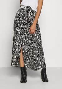 Sorte blomster maxi-nederdel med hvide margueritmønstre, med en slids foran og et let design. Båret med sorte ankelstøvler.