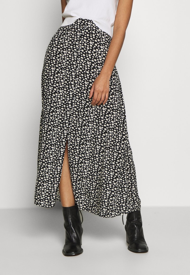 Sorte blomster maxi-nederdel med hvide margueritmønstre, med en slids foran og et let design. Båret med sorte ankelstøvler.