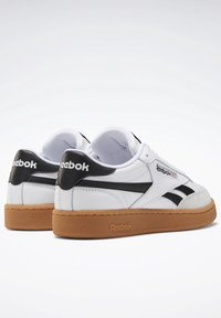 Bílé kožené tenisky s černými akcenty, které mají texturovanou gumu na podrážce a klasické logo Reebok na patě a bočních panelech.