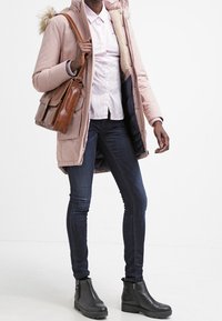 Roze, hoody parka met nep bont, gecombineerd met een gestreept shirt, donkere skinny jeans en zwarte enkellaarsjes. Bruine schoudertas.