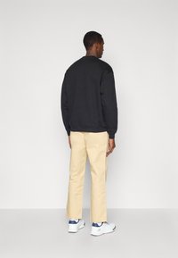 Melna svītra ar apaļu kakla izgriezumu, kombinēta ar bēšiem taisna piegriezuma biksēm un baltām sporta kedām. Apģērbs iezīmē minimālisma dizaina elementus.