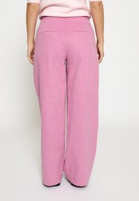 Lyserøde, vidde bukser lavet af et blødt, tekstureret stof. Har to baglommer og et rent, skræddersyet linning.