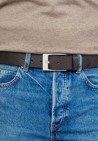 Mustat nahkahihna hopeisella suorakaiteen muotoisella soljella, joka on käytössä sinisten farkkujen päällä. näkyvissä ompeluaksentit ja hihnapidikkeet.