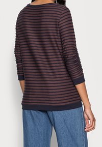 Maglietta a maniche lunghe a righe navy e bordeaux con texture a costine, scollatura rotonda e polsini aderenti. Vestibilità casual, con dettagli delle maniche leggermente arricciati.
