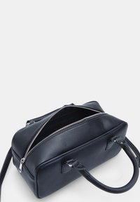 Sac à main en cuir noir avec double anses, surface texturée, fermeture éclair proéminente et intérieur spacieux. Conçu avec une forme rectangulaire.