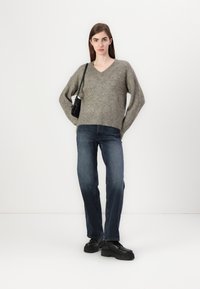 Grå, strukturert strikket genser med V-hals, sammen med mørkeblå, rette jeans og svarte snøresko. Veske hengt over venstre skulder.