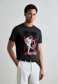 Black cotton T-shirt featuring a graphic print in red and white, depicting a figure with text "GUNS N' ROSES USE YOUR ILLUSION."