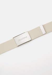 Cinto de tecido bege com fivela de metal prateado gravada com "Dickies" e um laço de metal ajustável em fundo branco.