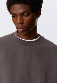 Dunkelgrauer Sweatshirt aus Baumwollmischung mit Rundhalsausschnitt und gerippten Abschlüssen. Glatte Textur mit minimalen Details.