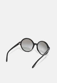 Óculos de sol redondos com uma armação preta brilhante e lentes graduadas em cinza. Apresenta braços elegantes e esguios com detalhes de marca discretos.