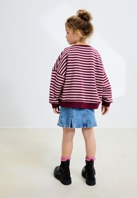 Bluza w paski w kolorze bordowym i różowym z opuszczonymi ramionami, zestawiona z jasną spódnicą z denimu. Czarne botki za kostkę z różowymi prążkowanymi skarpetkami.