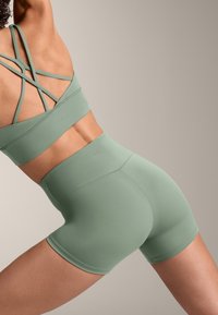 Zelená športová podprsenka a šortky s vysokým pásom, vyrobené z textúrovanej tkaniny, s prekríženými ramienkami a hladkým, priliehajúcim dizajnom.