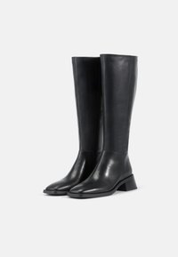 Μαύρες δερμάτινες μπότες μέχρι το γόνατο με λεία υφή, τετράγωνη μύτη και χοντρό τακούνι; διαθέτουν φερμουάρ στο πλάι για εύκολη χρήση.